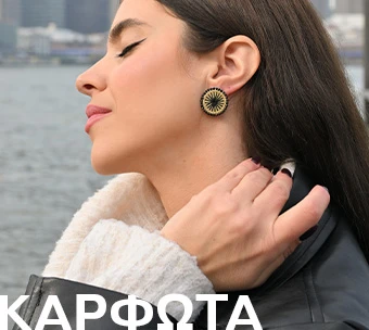 Γυναίκα με μακριά μαλλιά φορά εντυπωσιακά καρφωτά σκουλαρίκια με μοντέρνο σχέδιο,με φόντο εξωτερικό χώρο δίπλα στο νερό, δείχνοντας ιδεές για ένα ξεχωριστό δώρο.